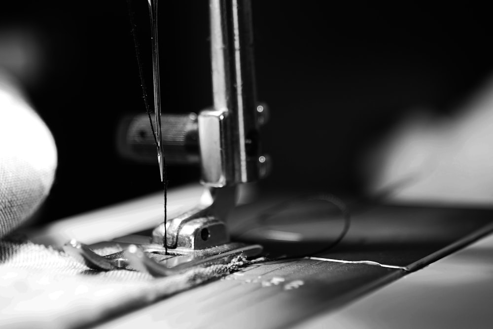 Black and white close-up of a sewing machine needle, presser foot, and threaded fabric