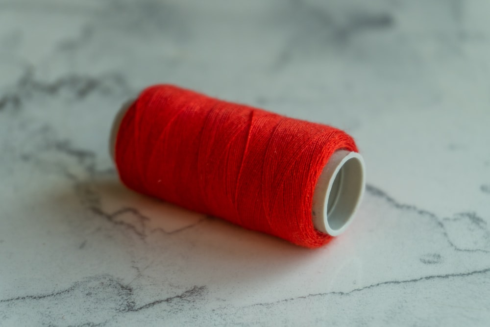 A spool of bright red thread lies on a light marble surface