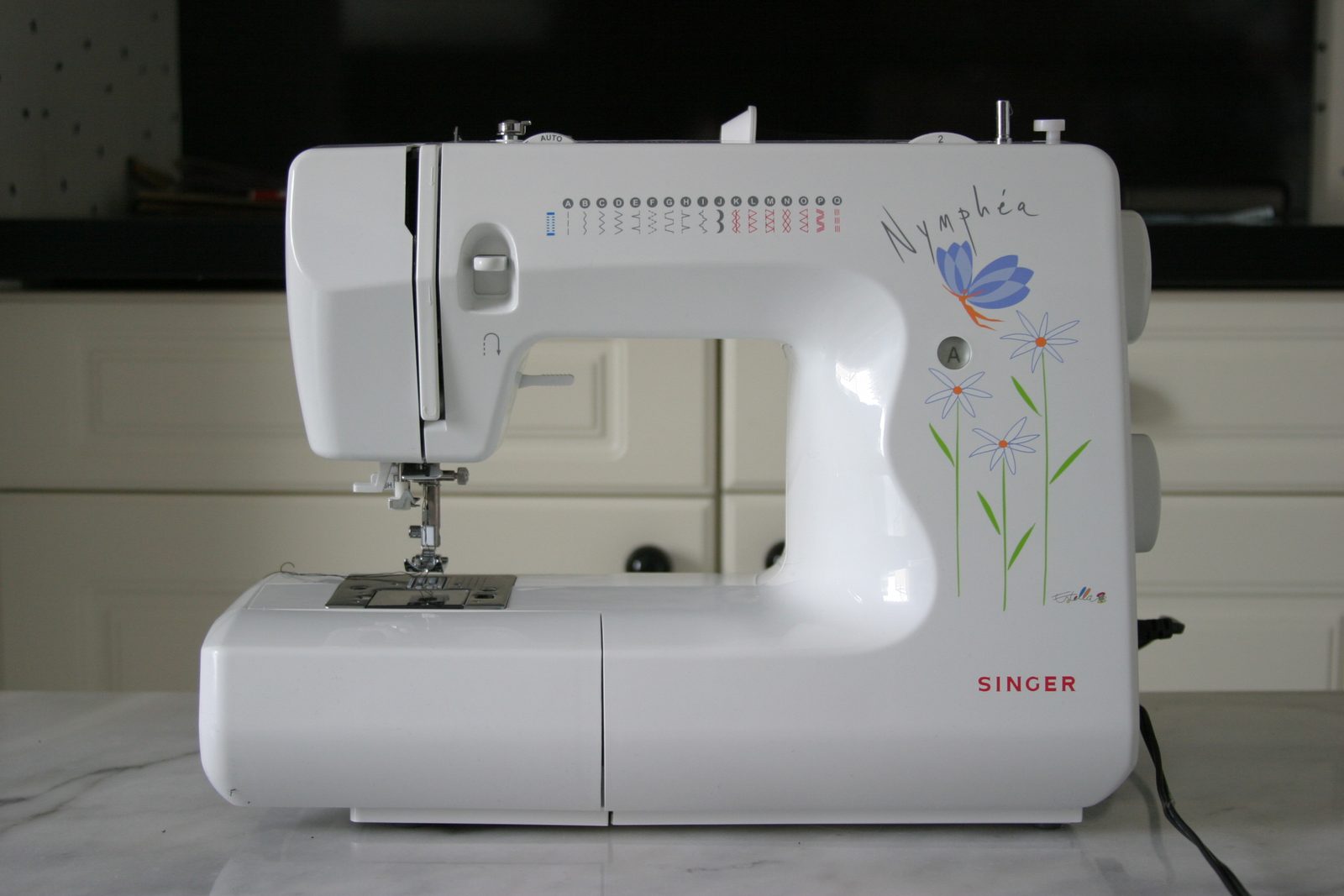 A white sewing machine with blue and green floral graphics rests on a table