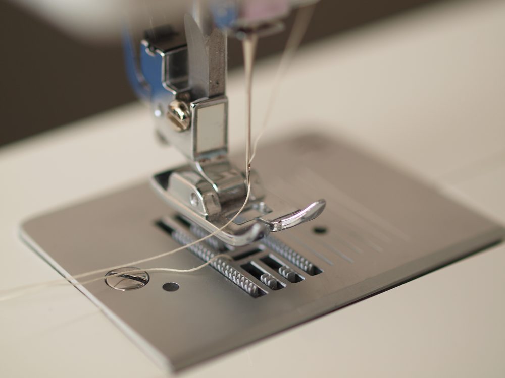 Close-up of a sewing machine presser foot and needle threaded with light thread
