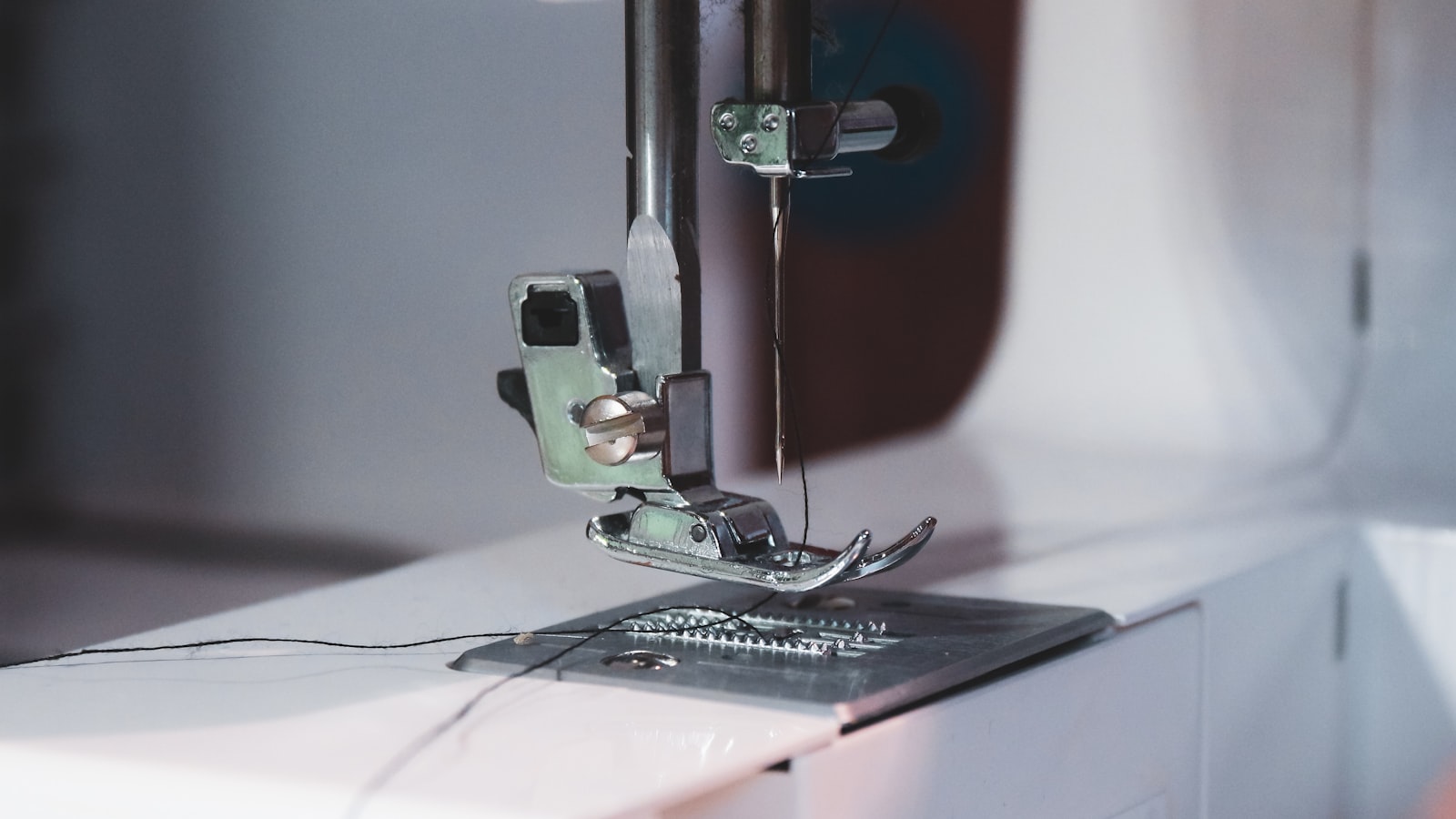 Close-up of a sewing machine needle and presser foot with dark thread