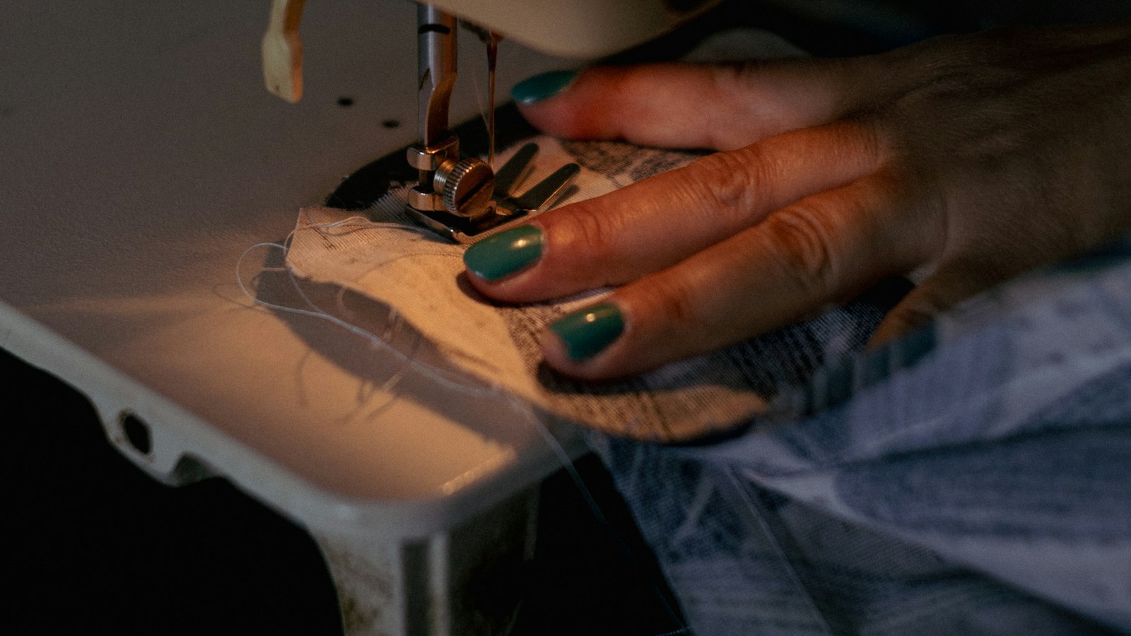A hand guides fabric under the needle of a sewing machine