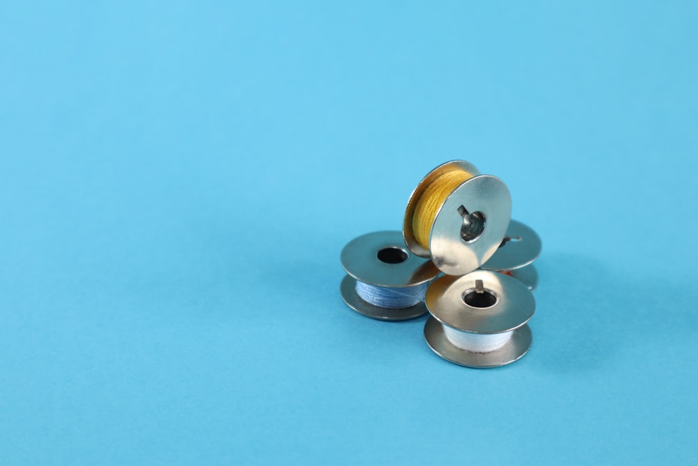 A small stack of four metal sewing bobbins wound with different colored thread on a blue surface