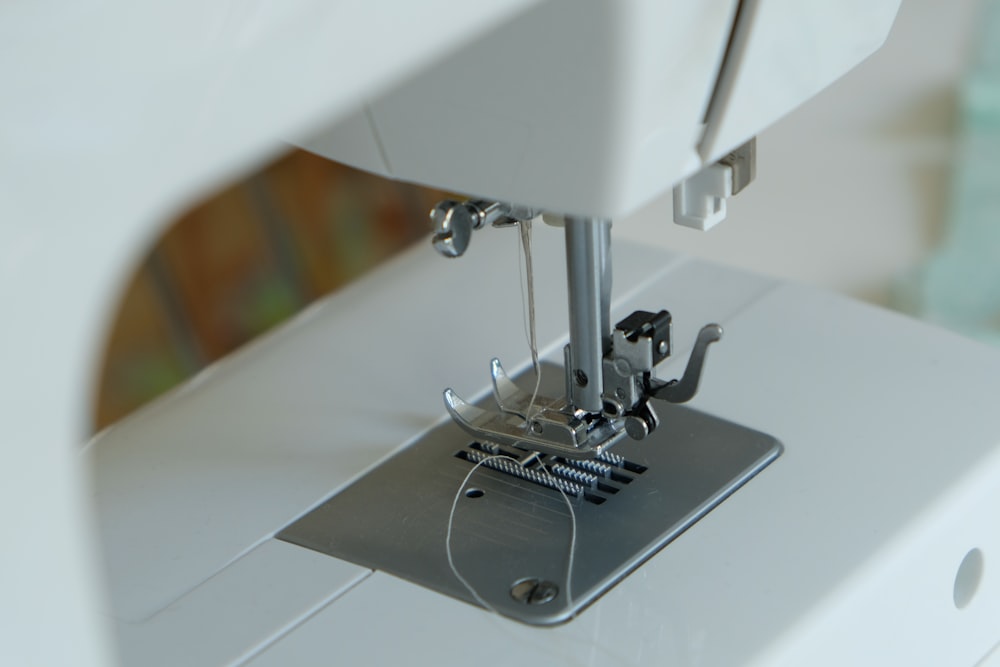 Close-up of a white sewing machine needle bar and presser foot with threaded needle