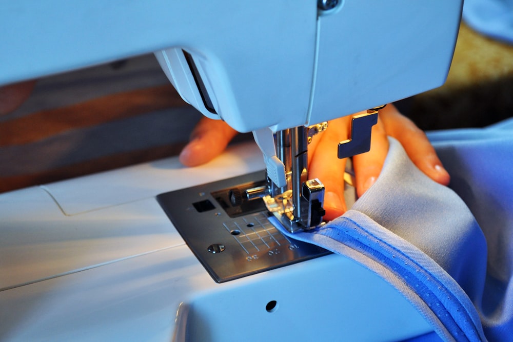 Hands guide blue fabric under the needle of a white sewing machine