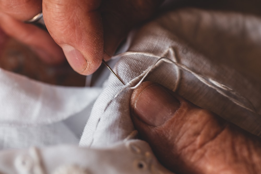 Close-up of hands sewing white fabric with a needle and thread