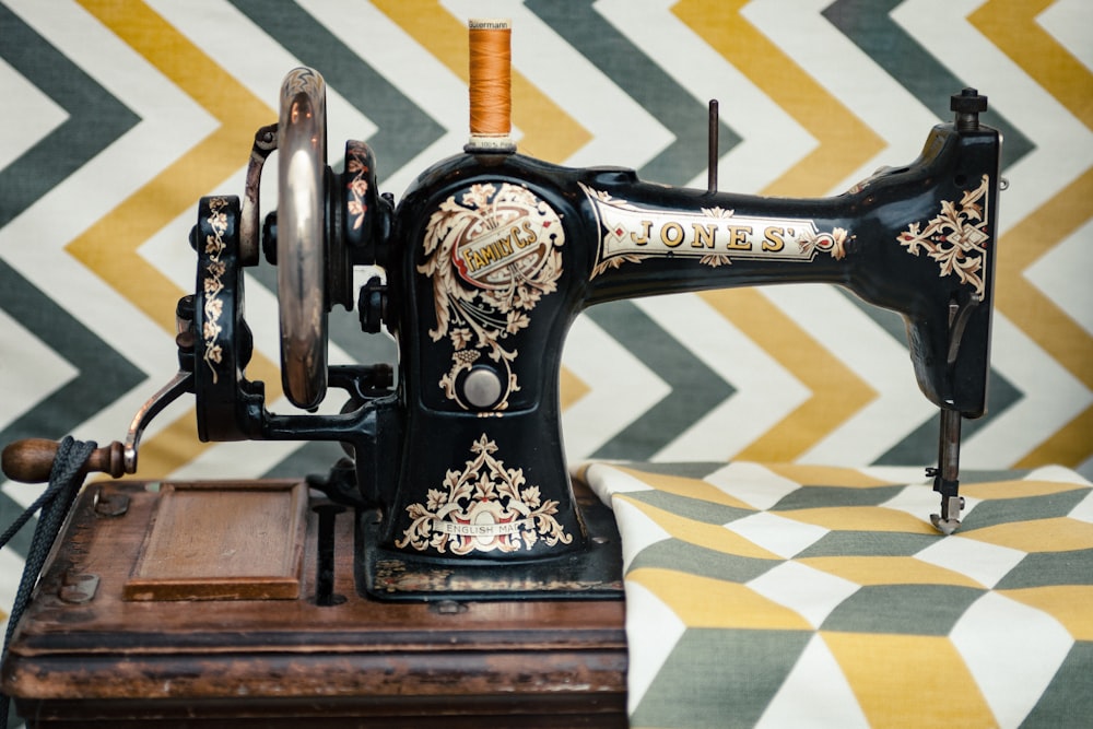 A vintage black sewing machine with gold floral decals rests on a wooden base with geometric fabric