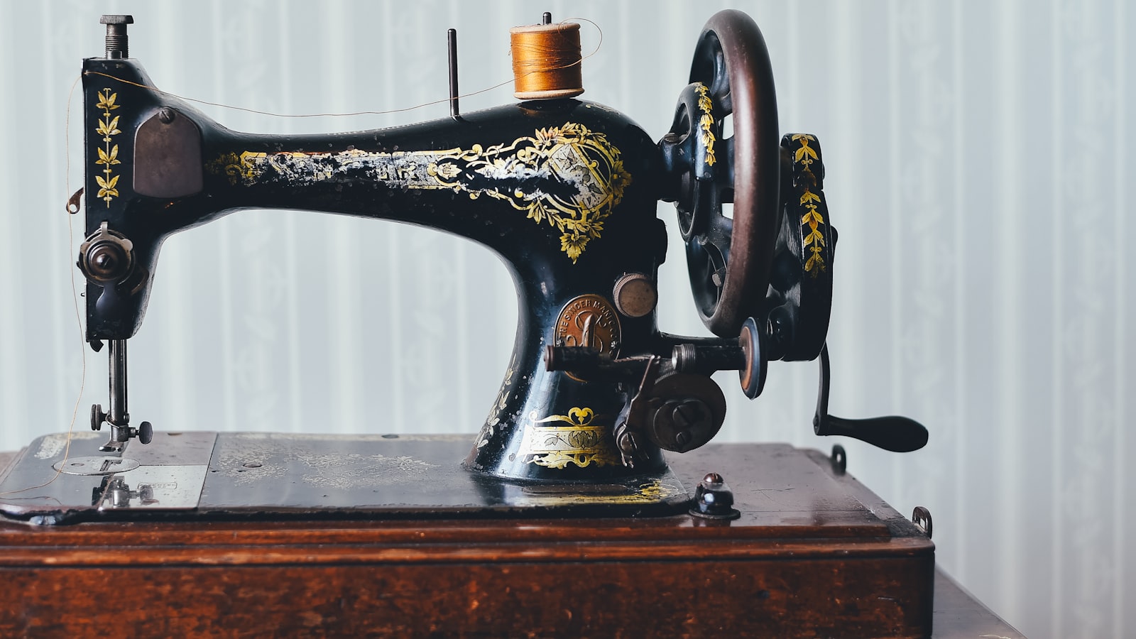 Vintage black sewing machine with gold floral decals rests on a wooden base