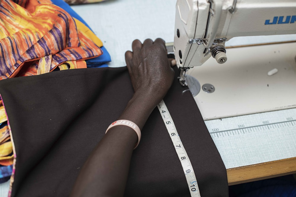 A person's hand guides brown fabric under the needle of a white sewing machine