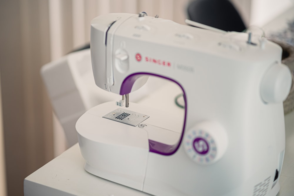 A white and purple sewing machine sits on a white table