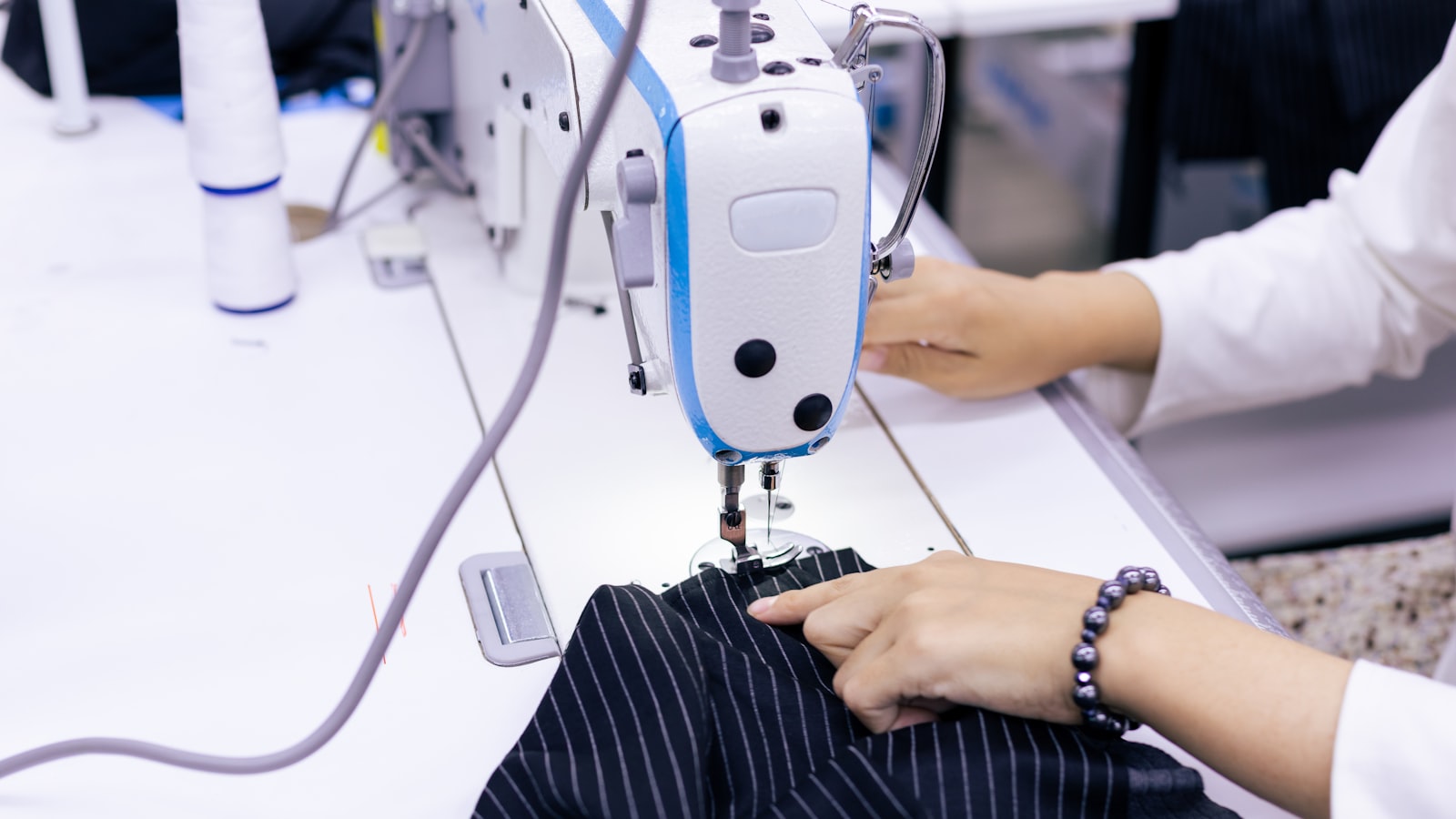 A person guides black striped fabric under the needle of an industrial sewing machine