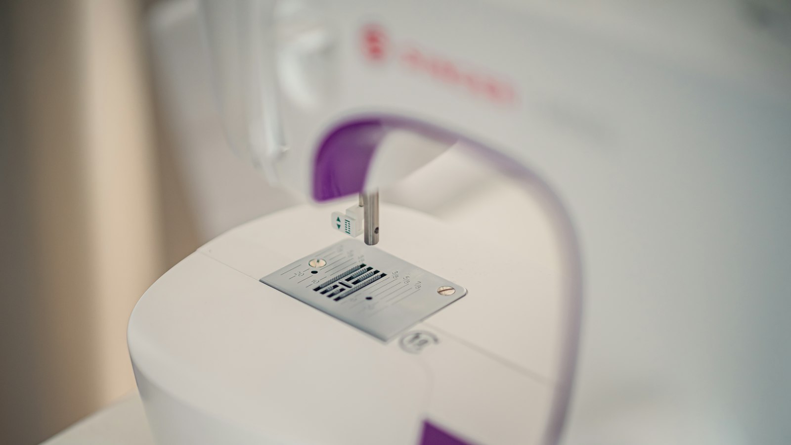 Close-up of a white sewing machine with purple accents and a metal needle plate