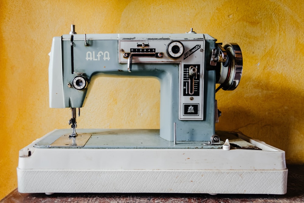 A vintage blue sewing machine sits on a white base against a yellow wall
