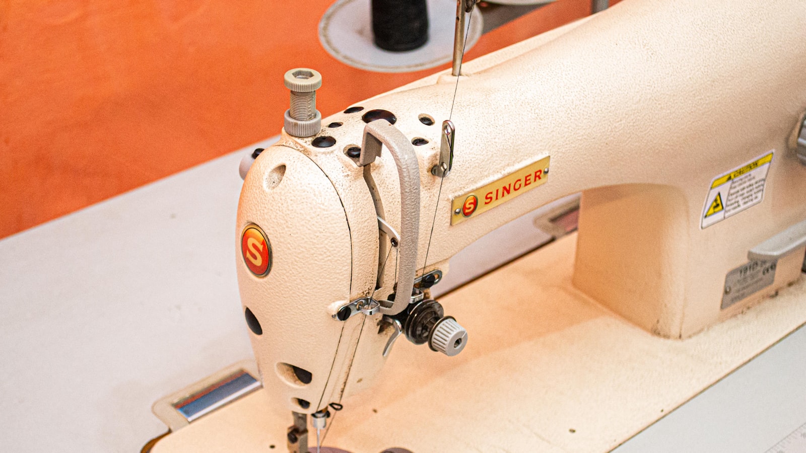 A Singer sewing machine sits on a table with a red wall in the background