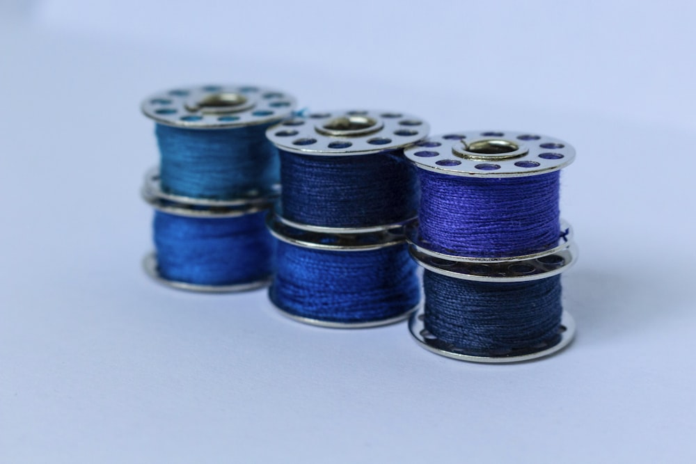 Three stacks of two metal sewing bobbins wound with blue thread