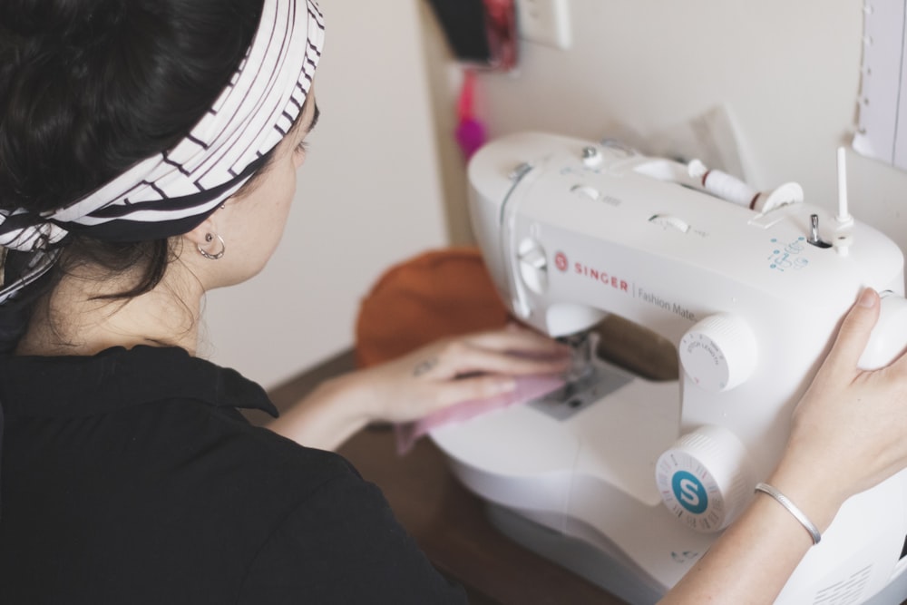 A woman with a patterned headband sews pink fabric with a white sewing machine
