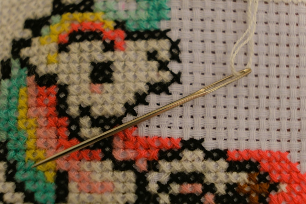 A needle threaded with white floss rests on a half-finished cross-stitch