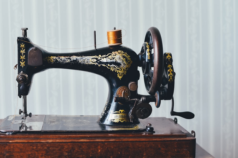 An antique black sewing machine with gold floral decals rests on a wooden base