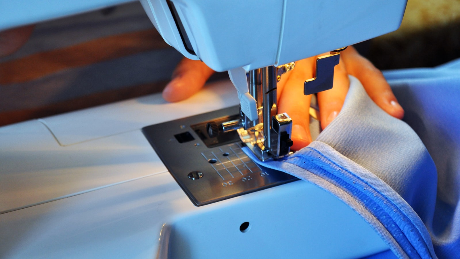 Hands guide light blue fabric through the needle area of a sewing machine