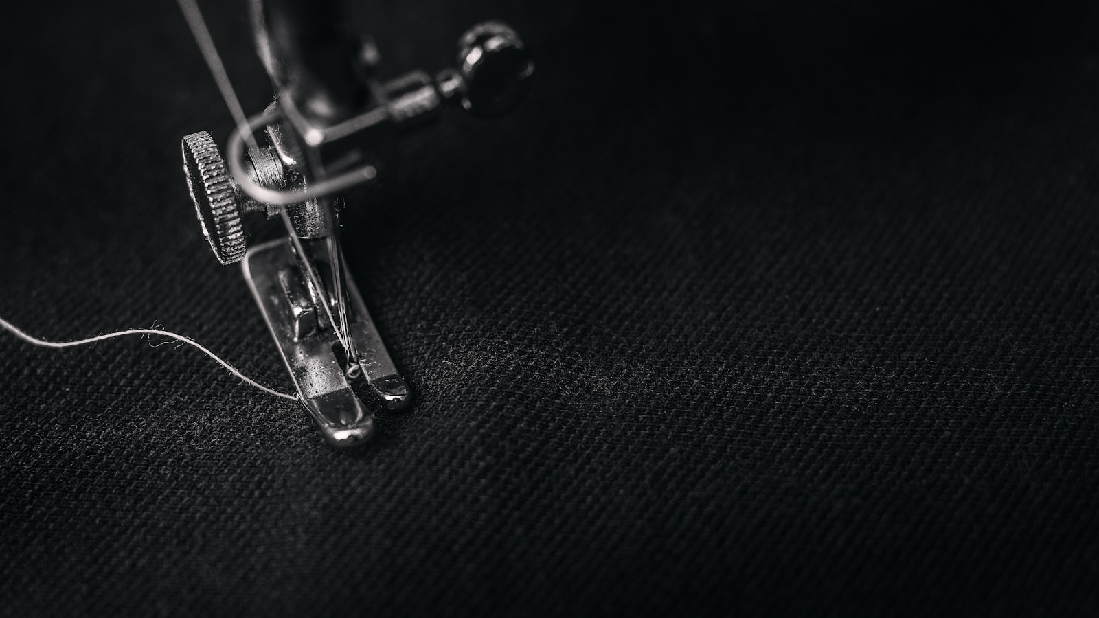 Close-up in black and white of a sewing machine needle and presser foot on black fabric