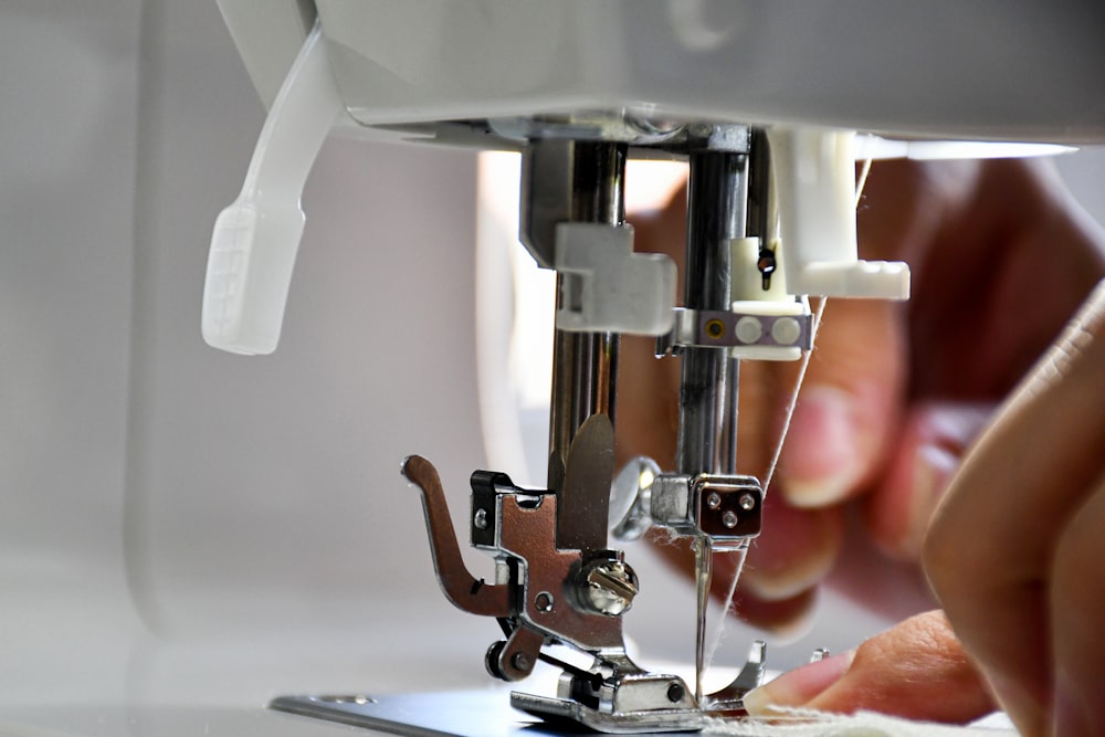 Close-up of a sewing machine needle, presser foot, and fingers guiding fabric underneath