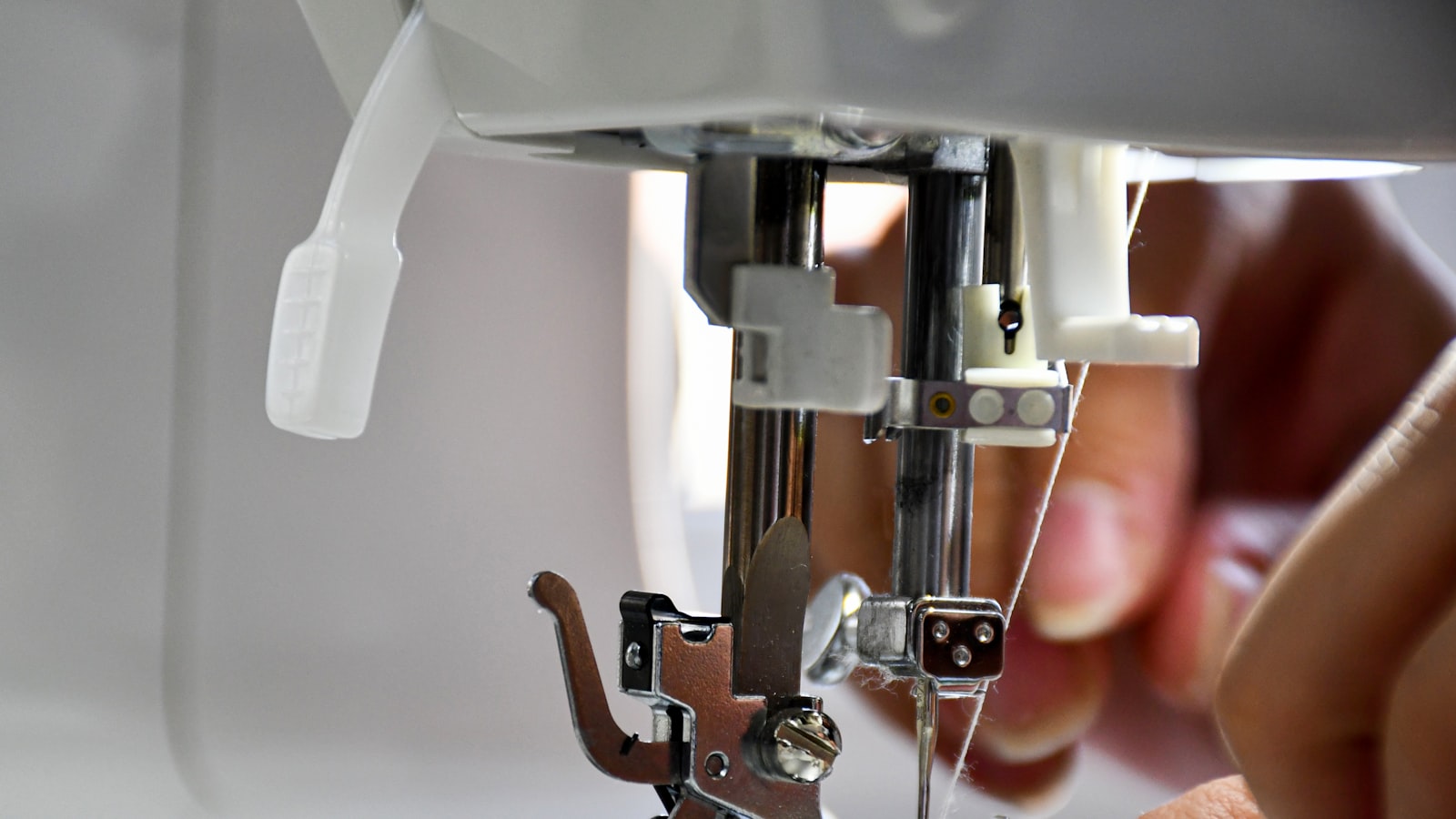 Close-up of a sewing machine needle mechanism with hands threading it