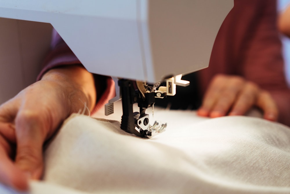 Close-up of a person guiding light-colored fabric through a white sewing machine