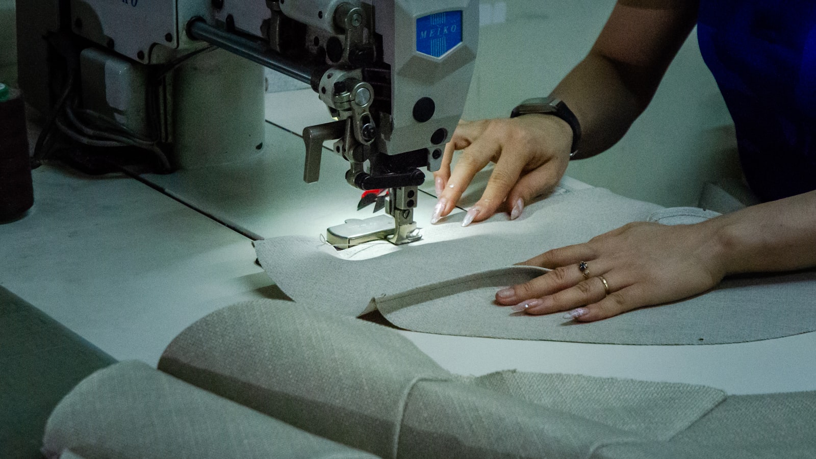 A person guides fabric with both hands under the needle of an industrial sewing machine