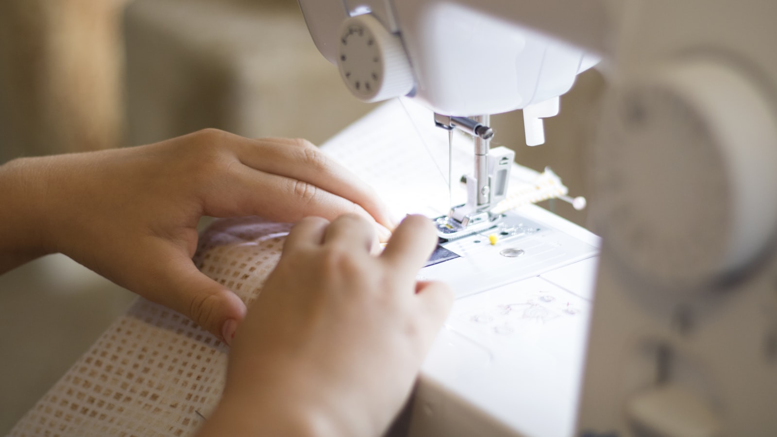 A person's hands guide patterned fabric under the needle of a white sewing machine
