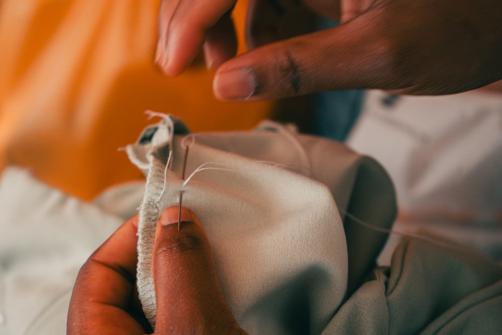 Hands use a needle and thread to sew a gray fabric