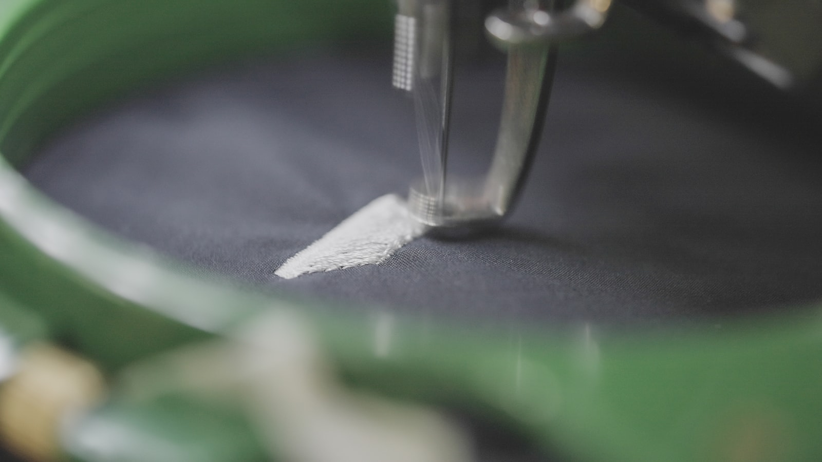 Close-up of a sewing machine needle stitching white thread onto dark fabric