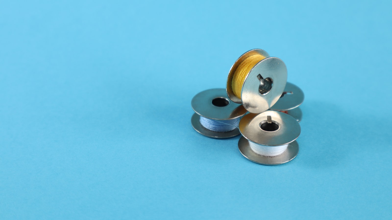 A small pile of sewing machine bobbins with different colored thread on a blue background