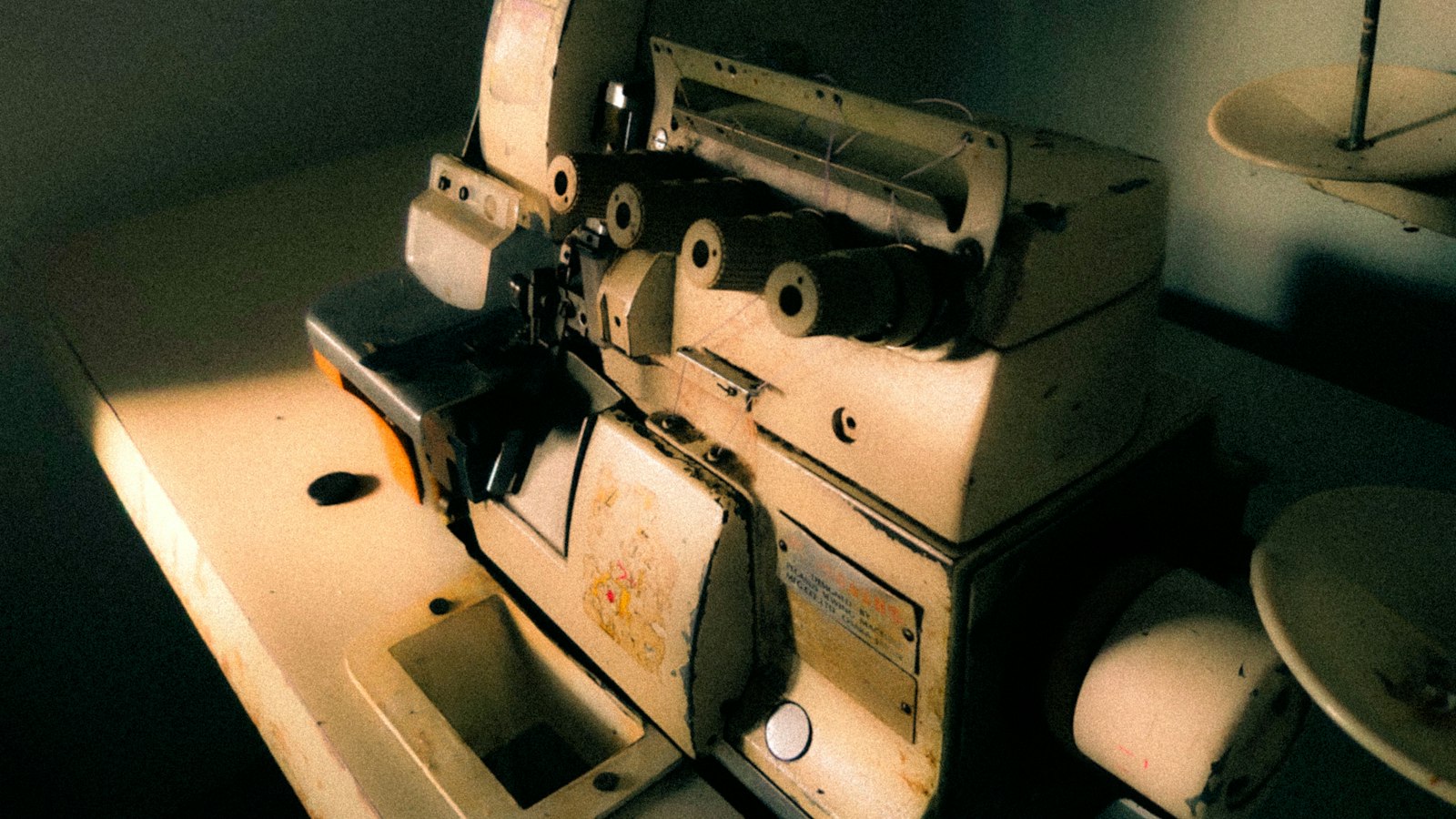 An old, beige-colored industrial serger machine sits on a worn table